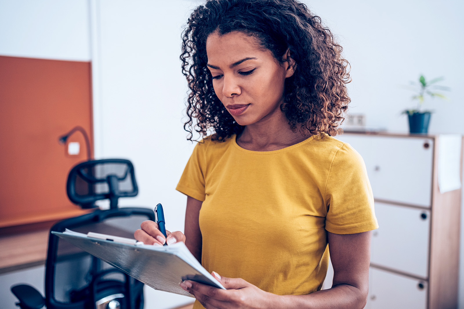 A Black businesswoman making notes on a clipboard inside of the office.