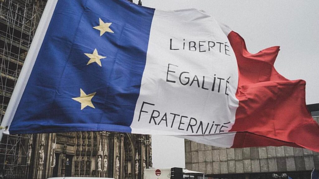 A French flag bearing the words liberté, egalité, fraternité waves in the wind