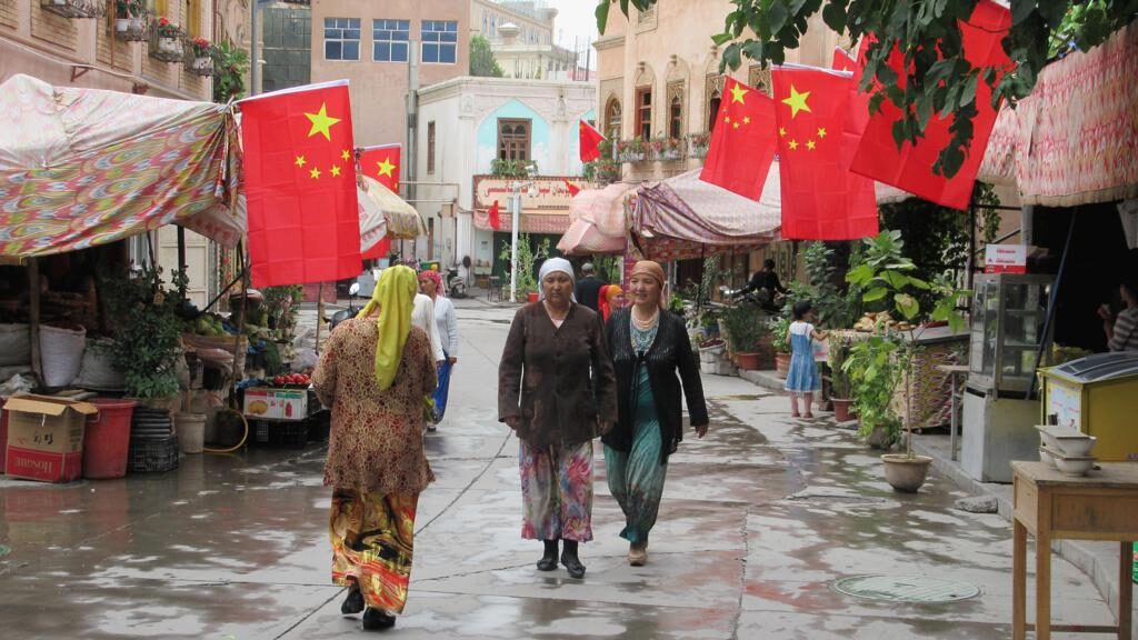 Photo of three women walking down a street under Chinese flags in Kashgar, Xinjiang, China