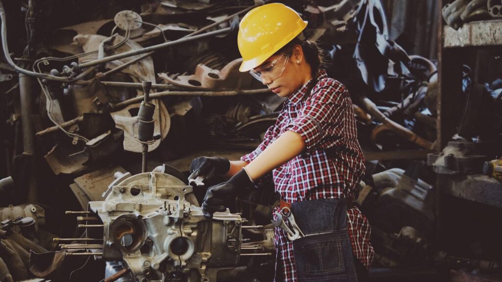 Photo of a young woman in a yellow safety helmet fixing a machine