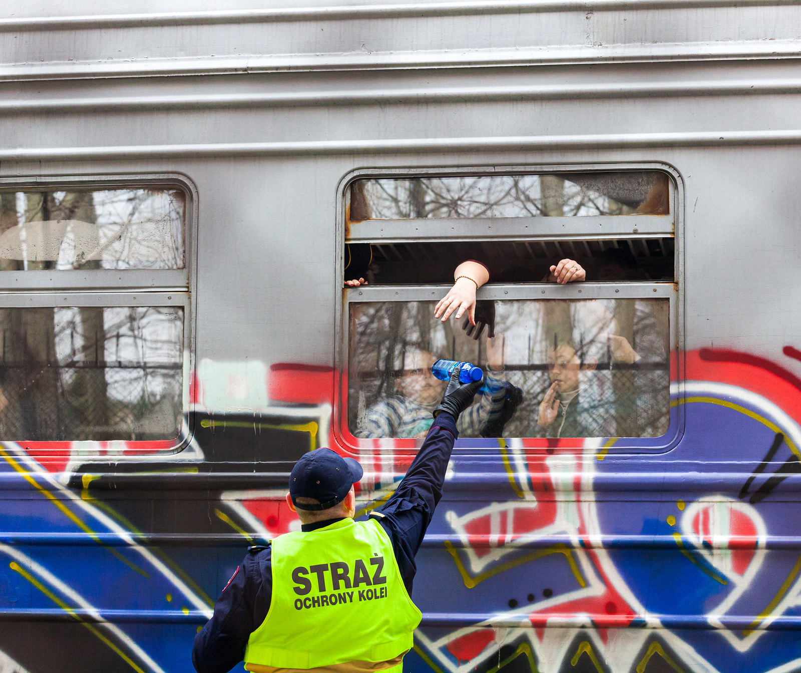 A man in a yellow safety vest hands bottled water to refugees inside a train