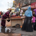 A woman sells strawberries from a cart on a rainy day. Two women and a little girl are clustered around the cart.