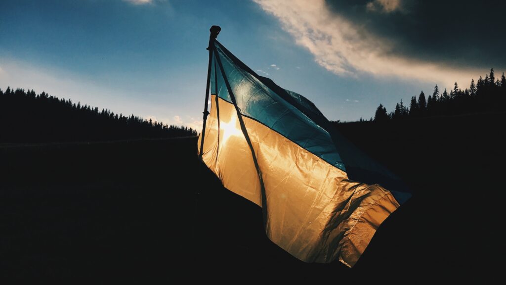 A Ukraine flag waves against a shadowed tree-filled hillside