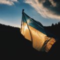 A Ukraine flag waves against a shadowed tree-filled hillside