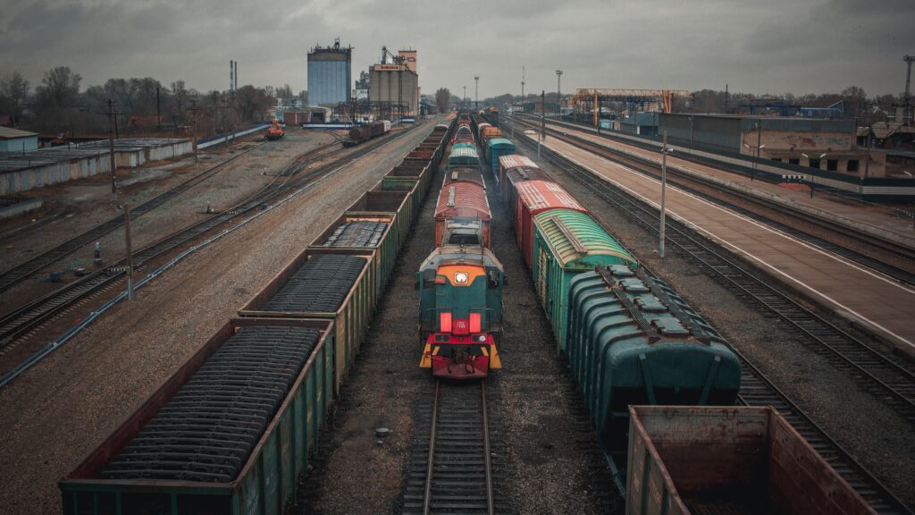 A train engine stands idle between two loaded freight trains in a train yard, on an overcast day