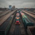 A train engine stands idle between two loaded freight trains in a train yard, on an overcast day