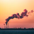 Photo of a factory emit a plume of smoke against the sunset