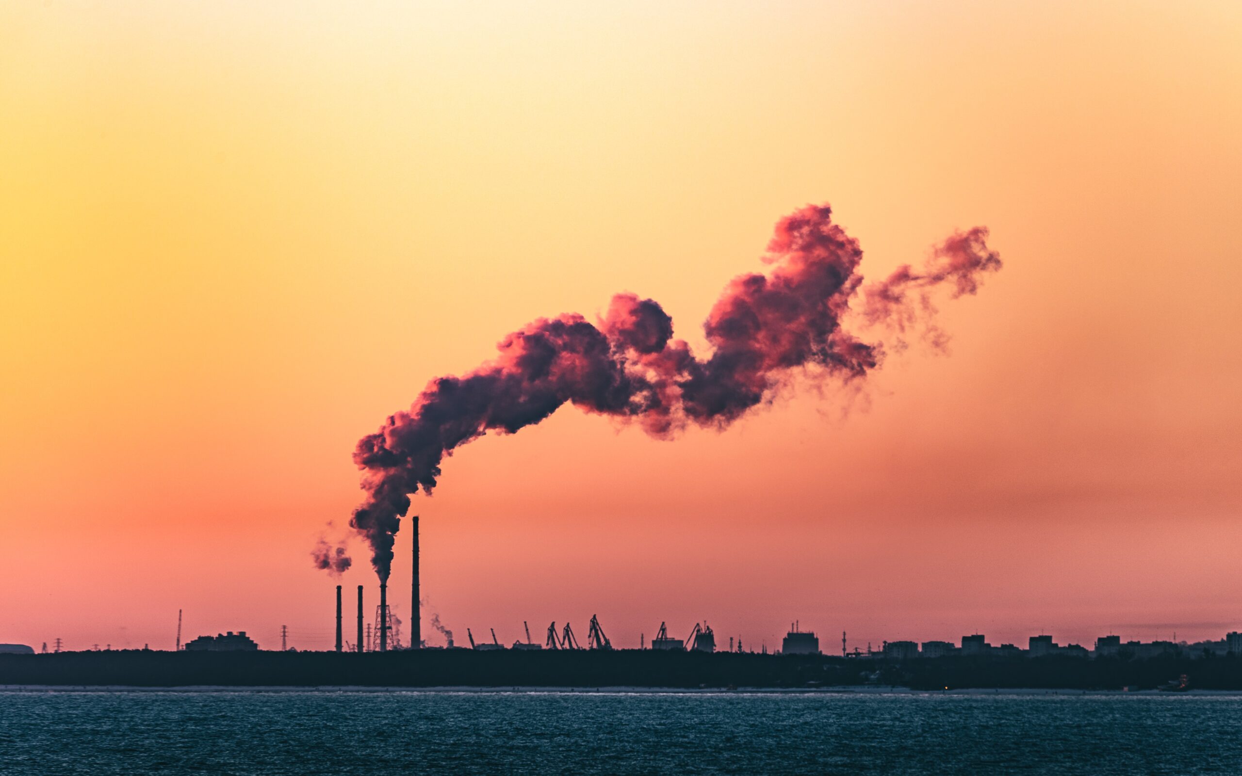 Photo of a factory emit a plume of smoke against the sunset
