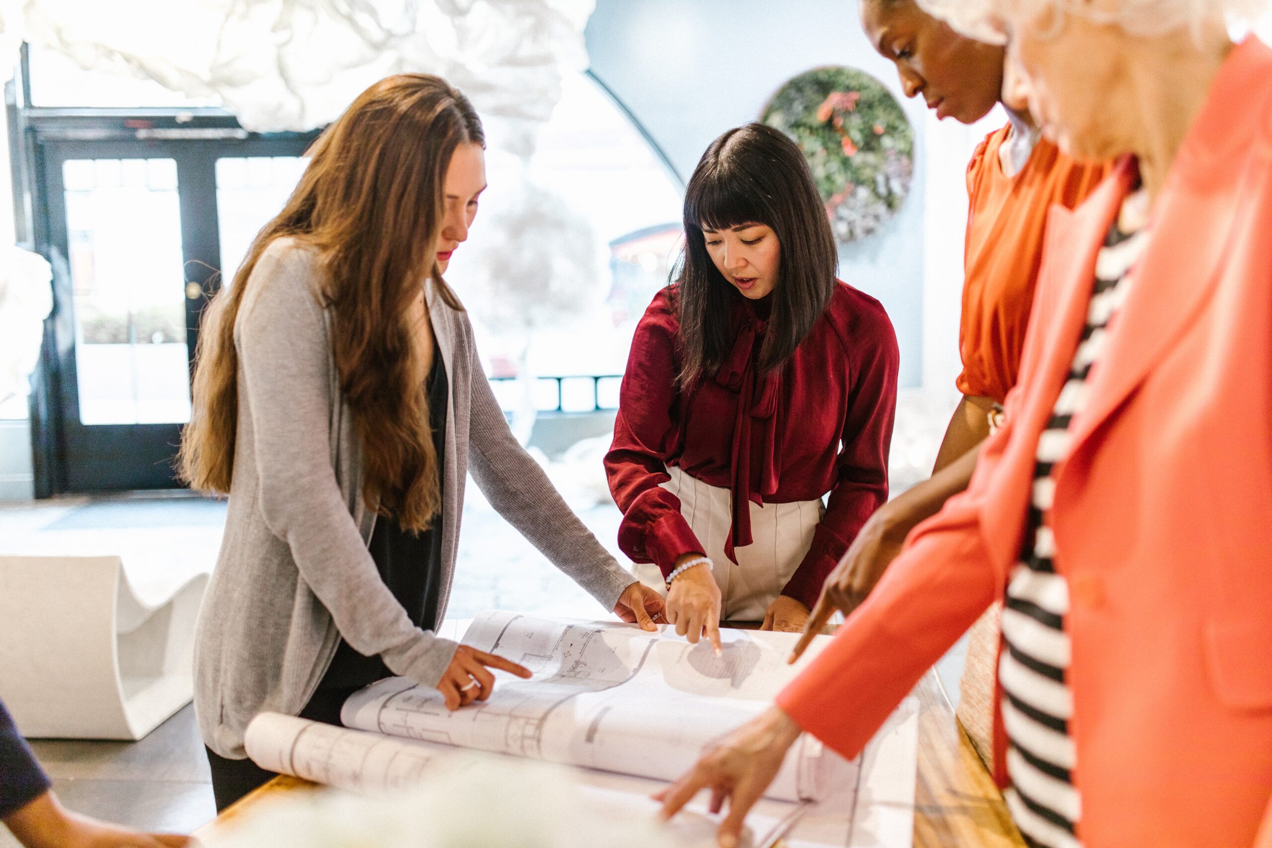 Four women stand around a table working, with their heads down.