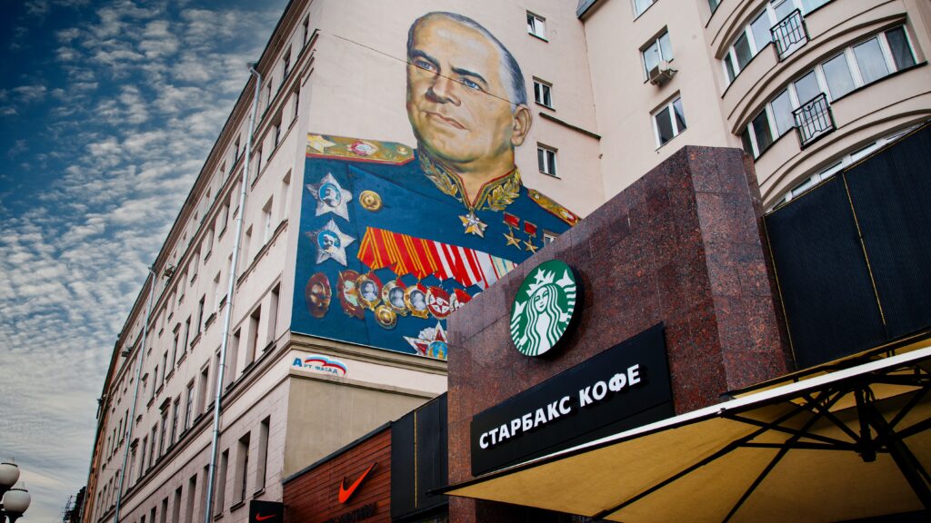 The outside of a Starbucks in Russia. The building next to the Starbucks has a graffiti mural of World War 2 Soviet general Georgy Zhukov