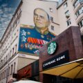 The outside of a Starbucks in Russia. The building next to the Starbucks has a graffiti mural of World War 2 Soviet general Georgy Zhukov