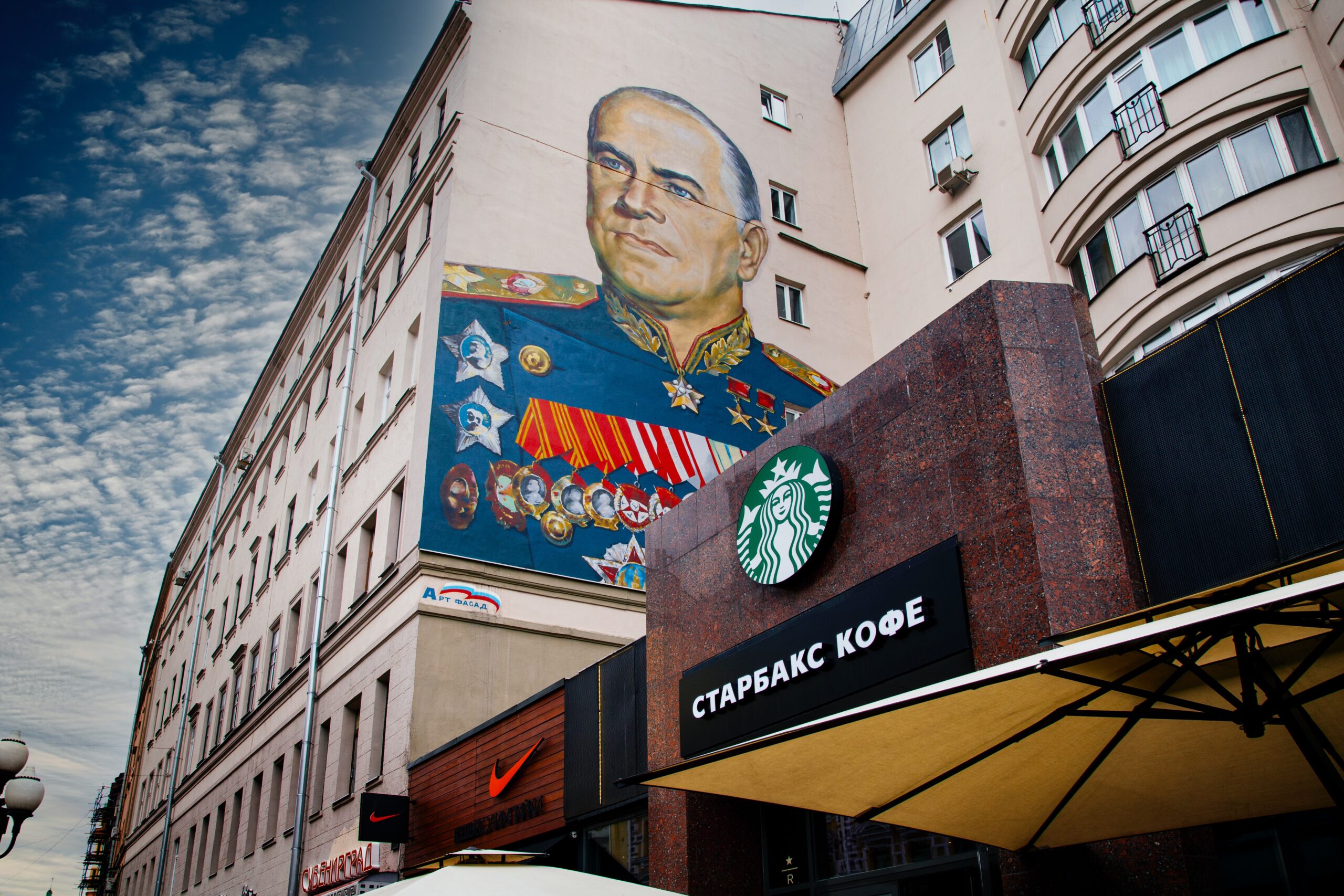 The outside of a Starbucks in Russia. The building next to the Starbucks has a graffiti mural of World War 2 Soviet general Georgy Zhukov