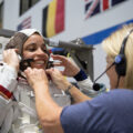 A smiling Black woman is helped into her NASA spacesuit by a blonde woman wearing a headset.