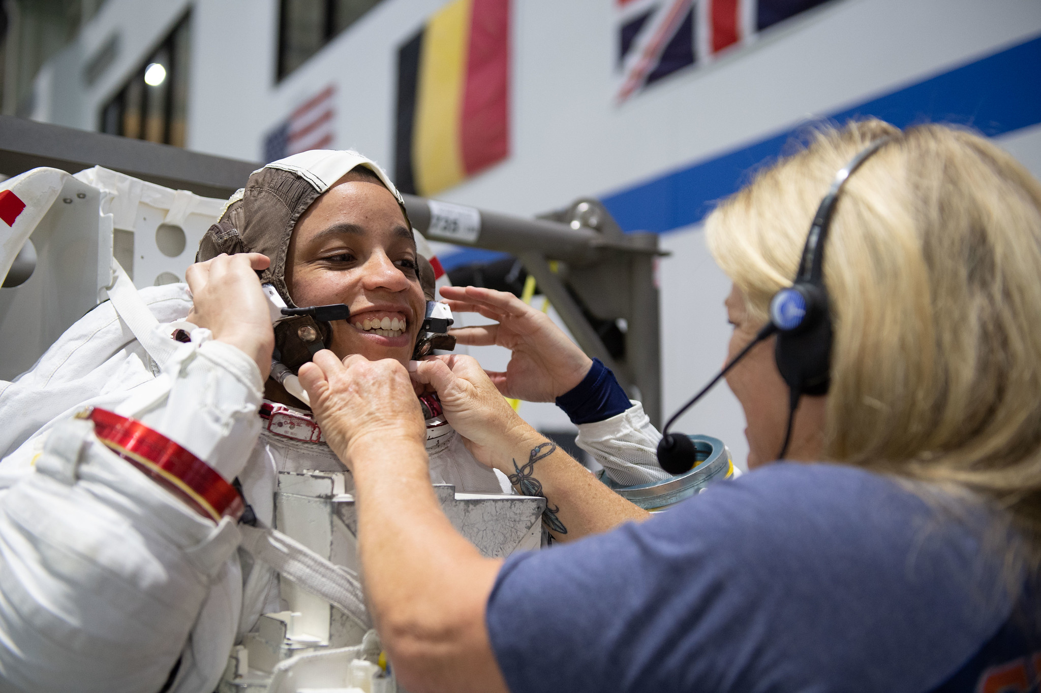 A smiling Black woman is helped into her NASA spacesuit by a blonde woman wearing a headset.