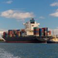 A container ship seen from behind on the ocean on a sunny day, carrying containers.