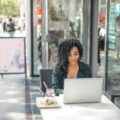 A person sits at a table on a sidewalk and works on her computer.