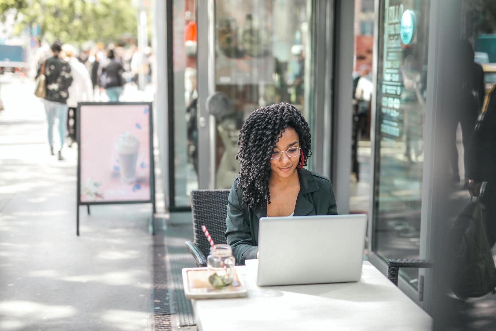 A person sits at a table on a sidewalk and works on her computer.