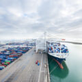 An aerial view of a container ship docked at port, with colorful containers waiting to be loaded onboard.