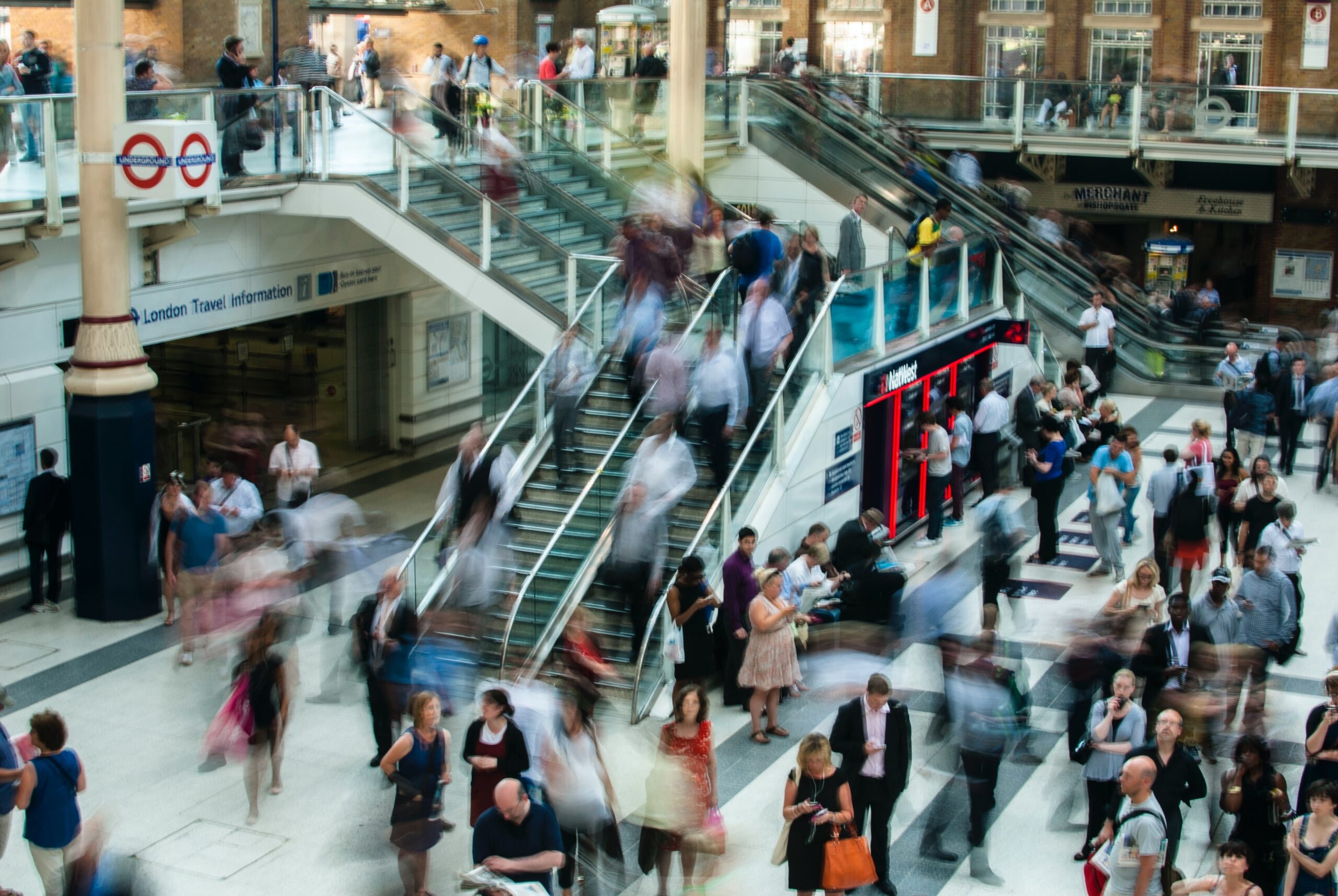 The inside of a British train station, with shops and blurred people moving around