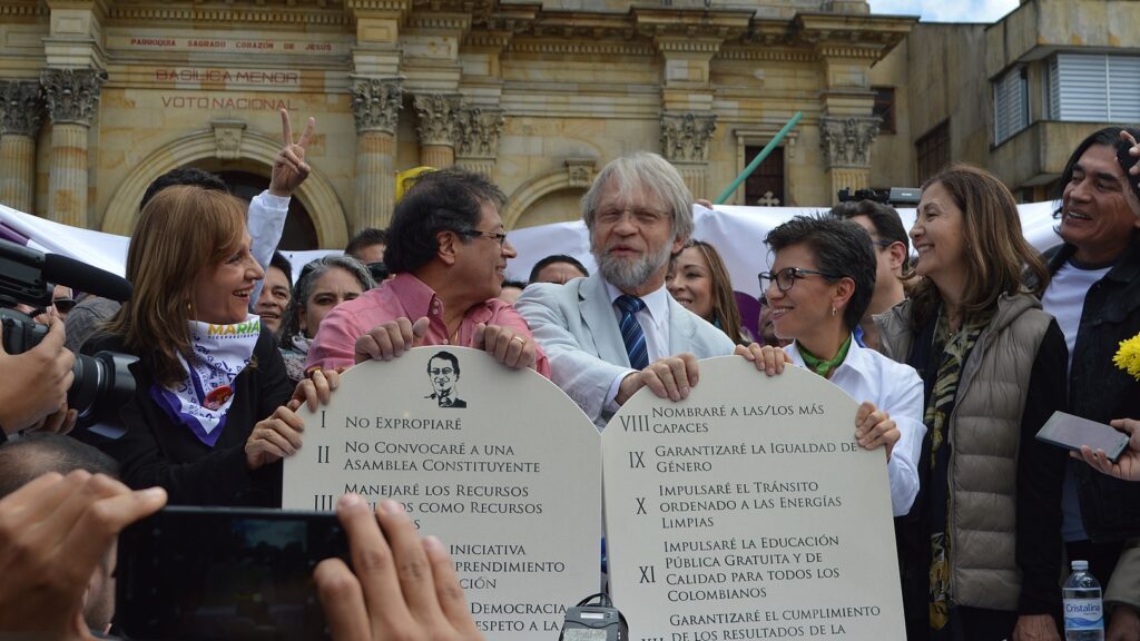 Two men stand next to each other holding up two paper tablets with laws written in spanish. A crowd surrounds them.