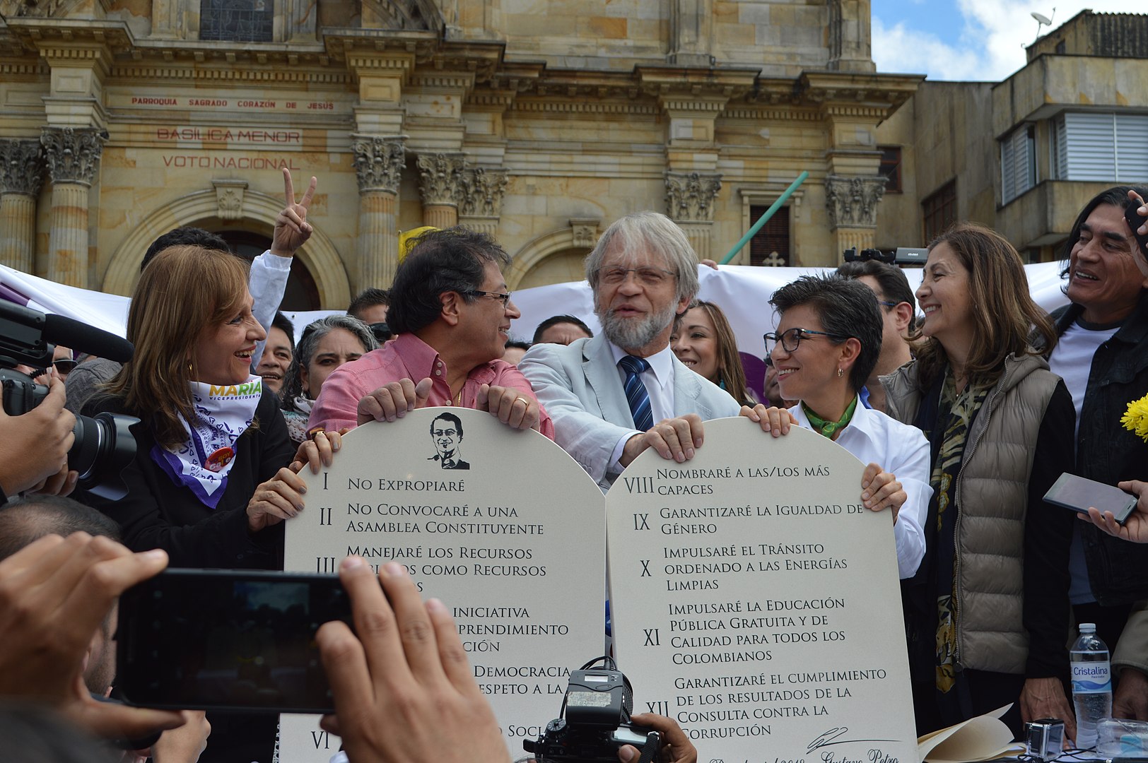 Two men stand next to each other holding up two paper tablets with laws written in spanish. A crowd surrounds them.