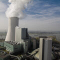 A gray power plant, seen from above, emits a plume of white smoke.