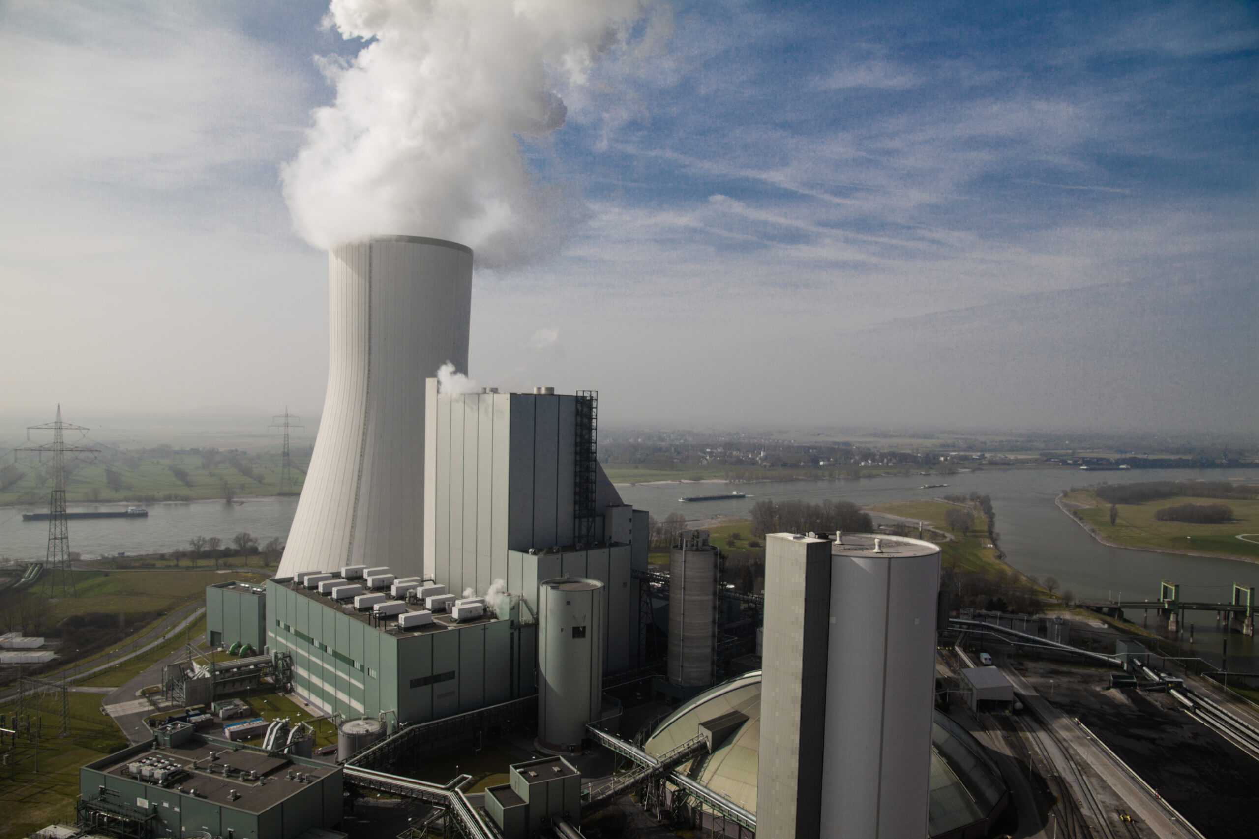 A gray power plant, seen from above, emits a plume of white smoke.