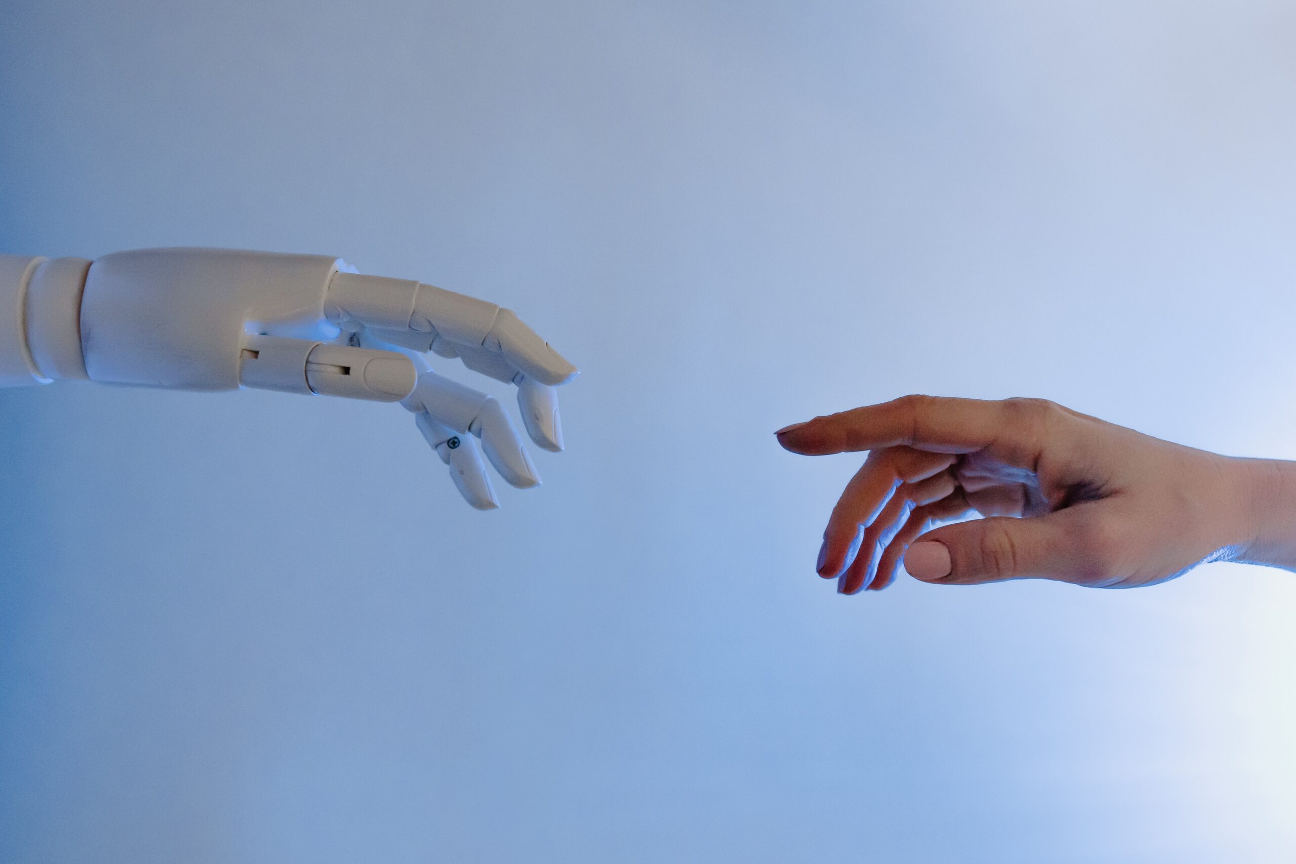 A robot hand and a human hand reach for each other against a light blue background.