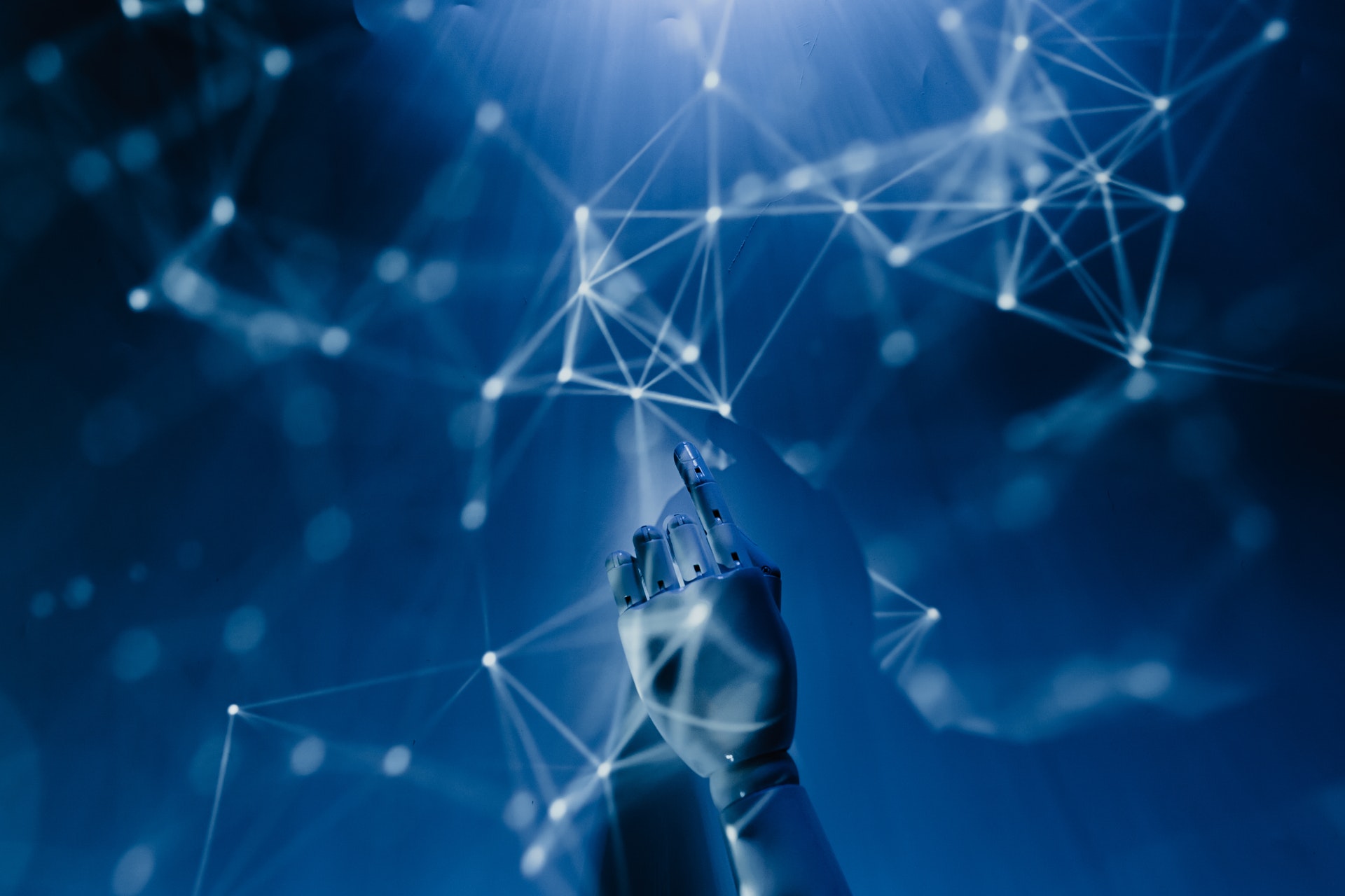 A robot hand reaches up with its forefinger extended. Geometric shapes are projected on a dark blue background.