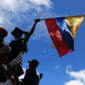 A silohuette of three people seen from below, holding the flag of Ecuador.