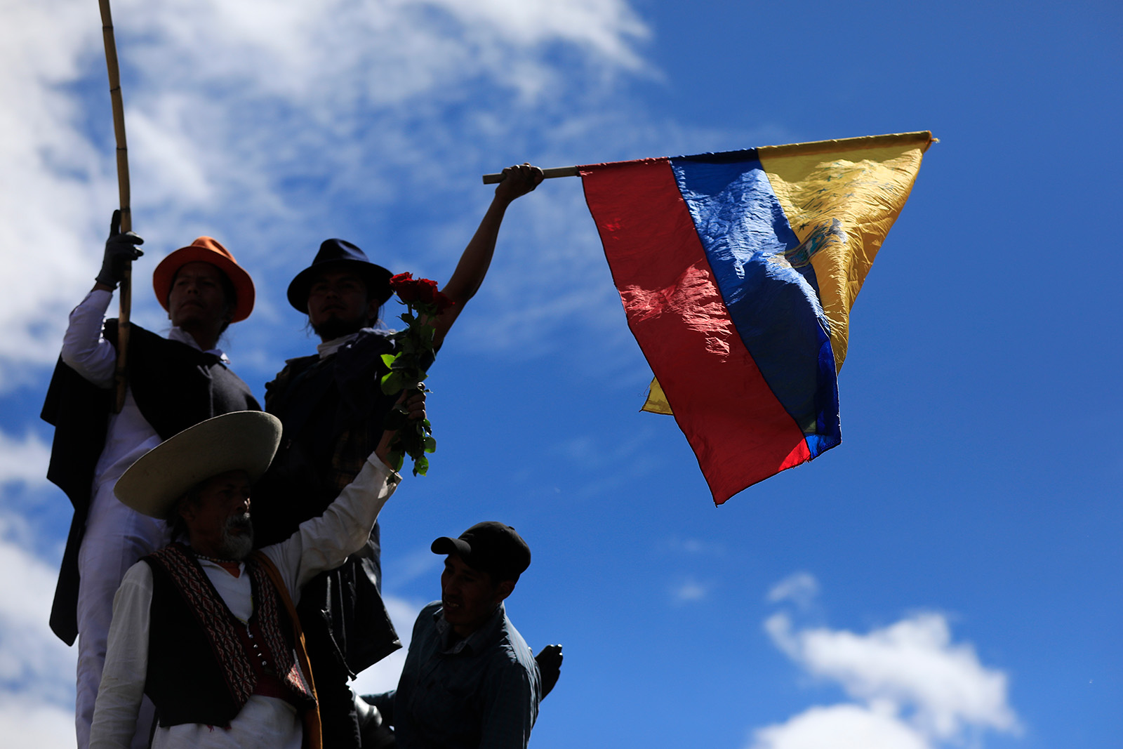 A silohuette of three people seen from below, holding the flag of Ecuador.
