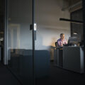 A business man sits in a dark office alone, with one light on above him.