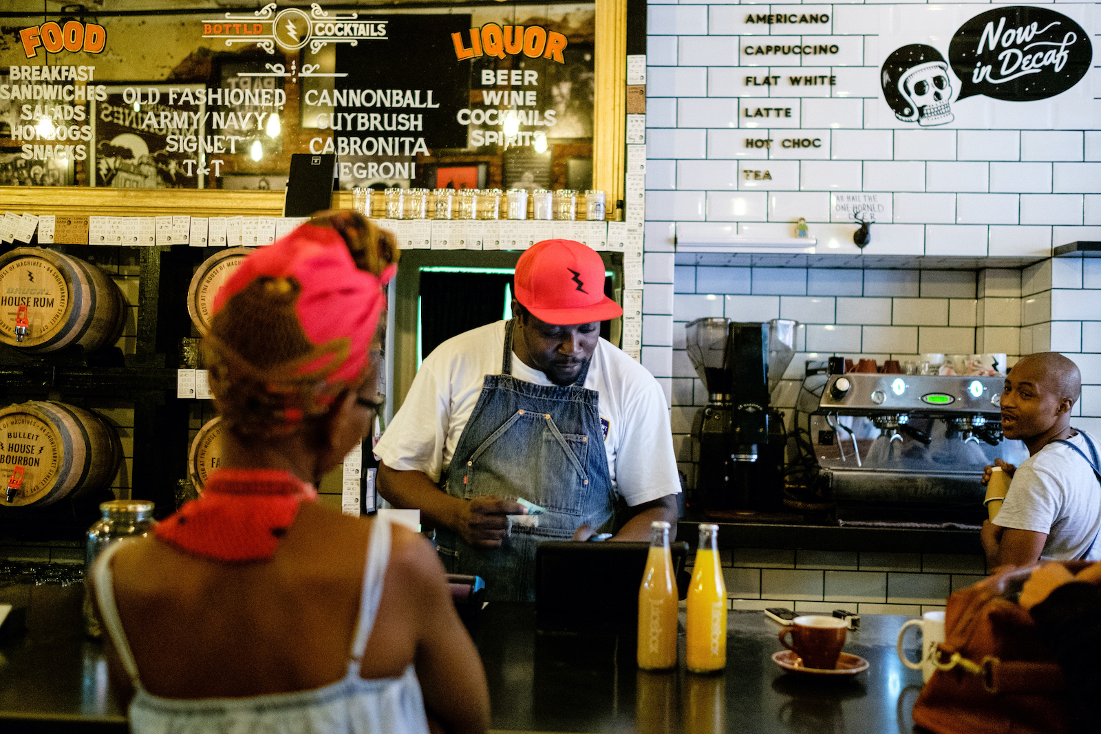 A barista behind a counter makes coffee, while a woman waits at the cash register for it.