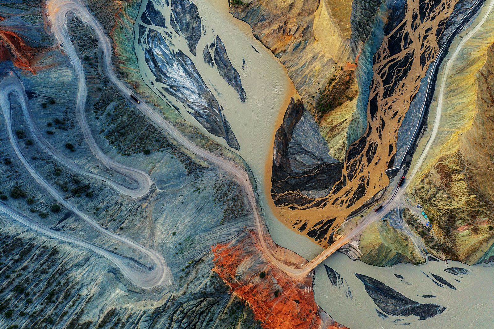 An aerial view of a road winding through colorful mountains. A mining truck can be seen driving on the road.