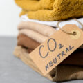 A stack of folded sweaters in earth tones. A cardboard tag says CO2 neutral.
