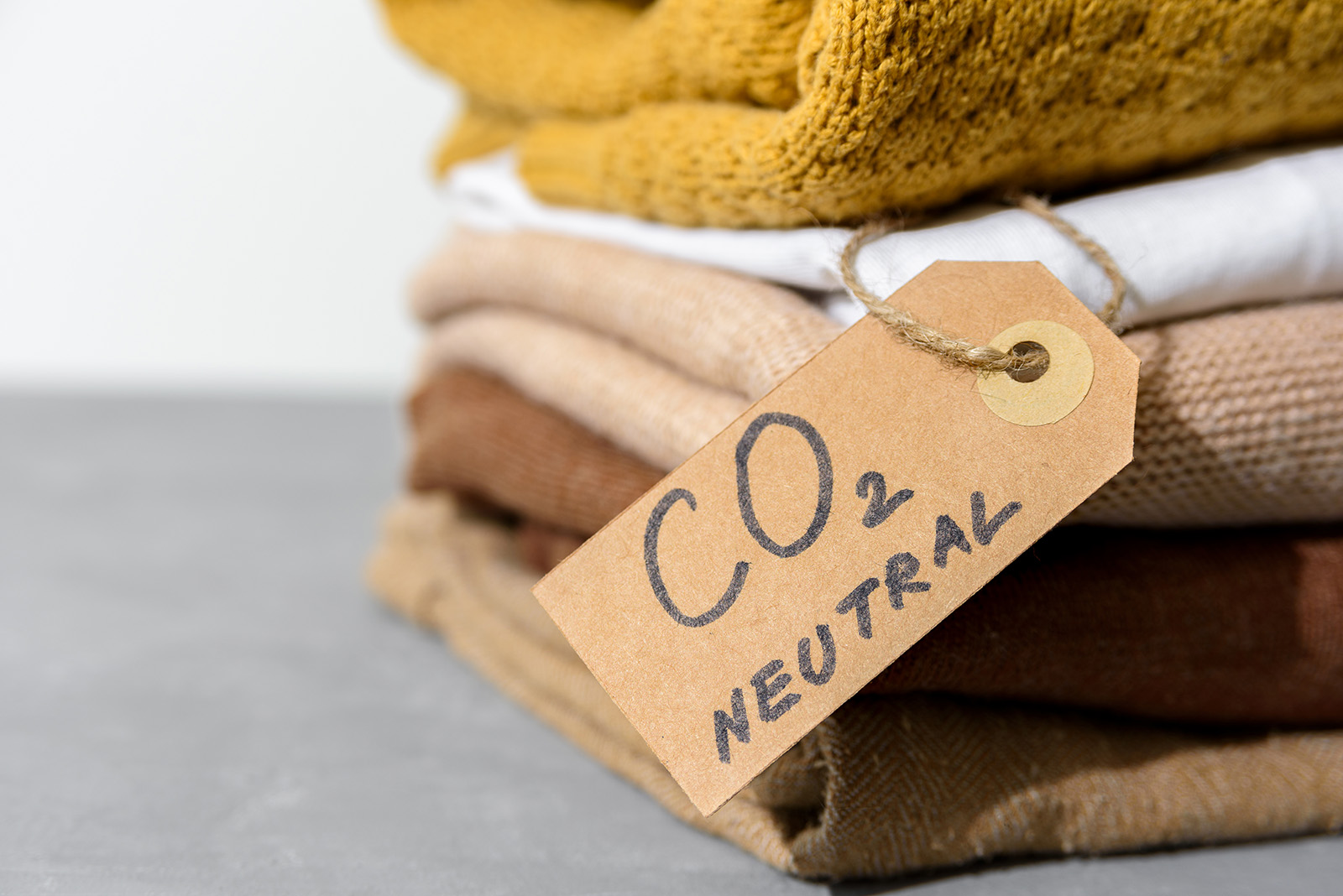 A stack of folded sweaters in earth tones. A cardboard tag says CO2 neutral.