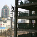 A man stands on scaffolding next to a construction site. In the background are tall buildings.