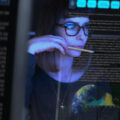 An employee works at her computer with images of data overlaid to imply surveillance.