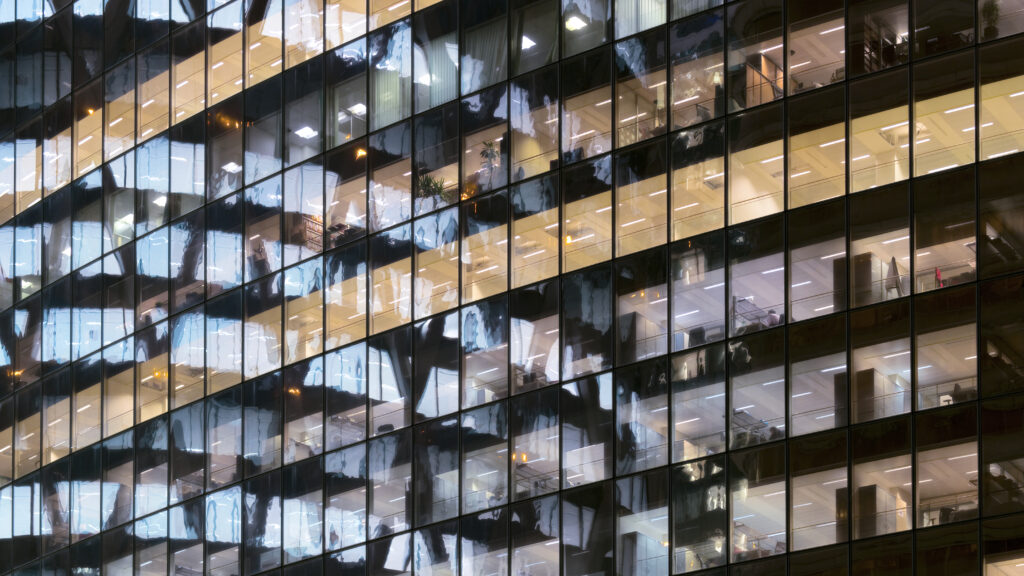 A office building is reflected in a window at night, with lit windows.