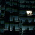 An employee, working late, is seen in an illuminated window of an office building that is otherwise dark.