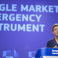 A woman in a blue dress stands behind a blue podium that says 