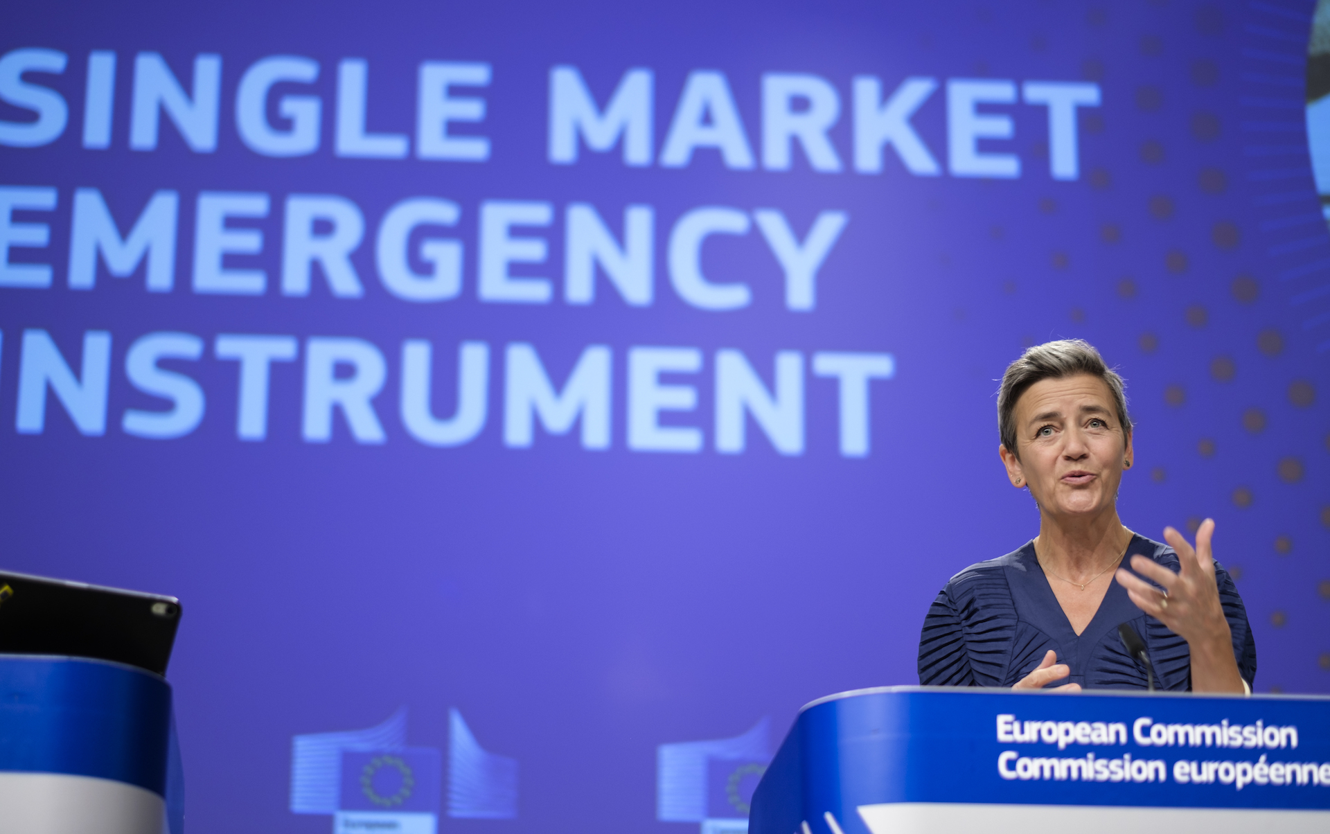 A woman in a blue dress stands behind a blue podium that says