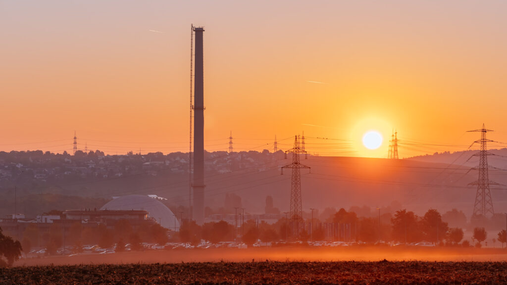 The sun sets behind a German nuclear plant, with chimneys in the hazy foreground.