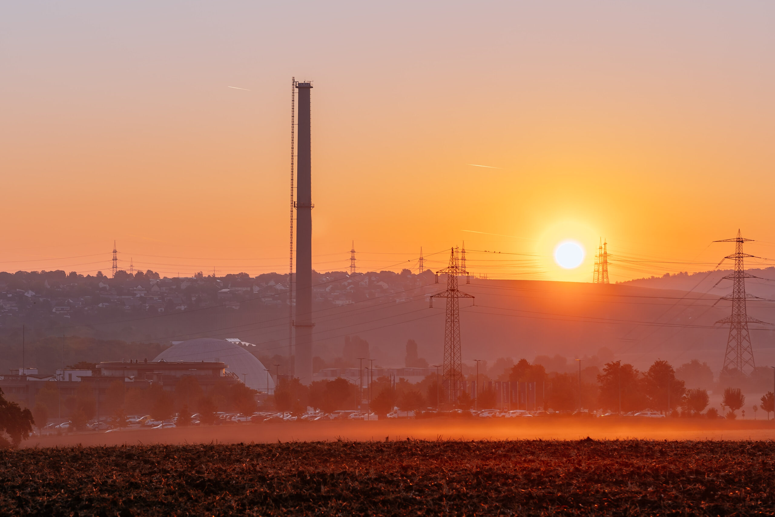 The sun sets behind a German nuclear plant, with chimneys in the hazy foreground.
