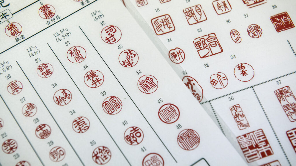 Two white sheets of paper are covered in vertical rows of red circular stamps, with Japanese characters.