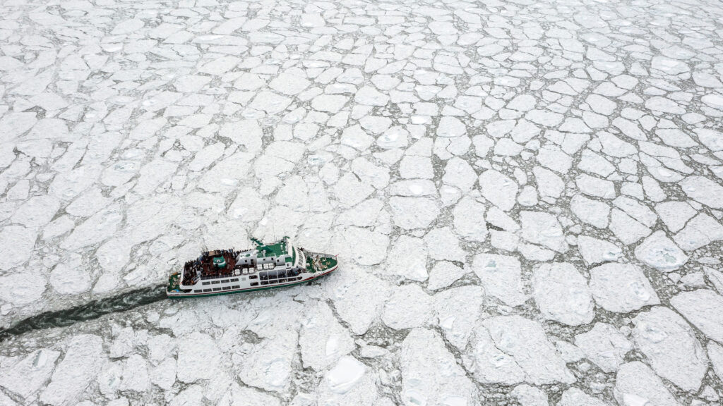 A boat seen from above. The boat is sailing through a vast sea of broken ice floes.