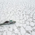 A boat seen from above. The boat is sailing through a vast sea of broken ice floes.