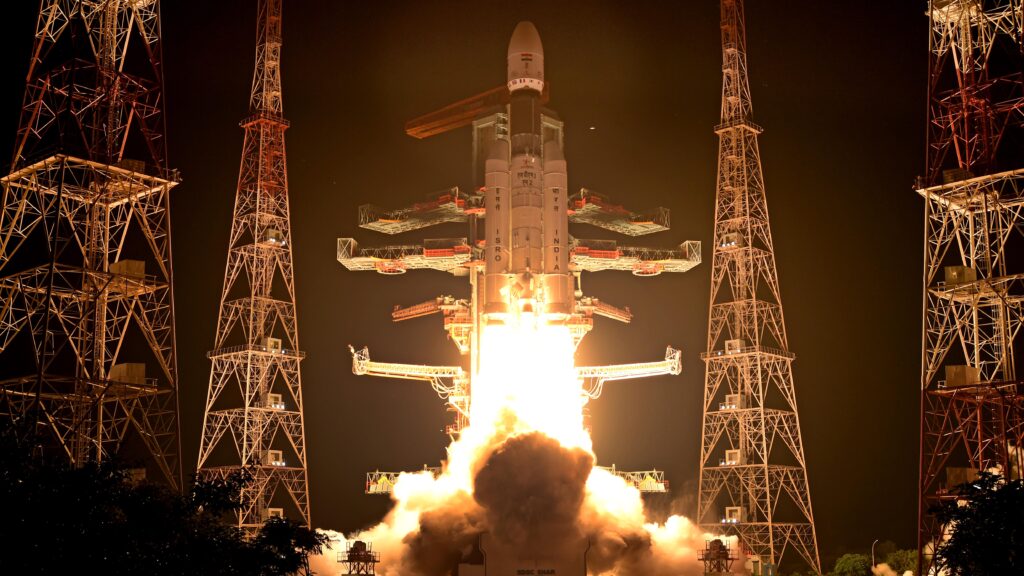 A rocket launches into space at night. The picture is mostly dark, with a white launch vehicle blasting off.