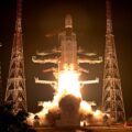 A rocket launches into space at night. The picture is mostly dark, with a white launch vehicle blasting off.