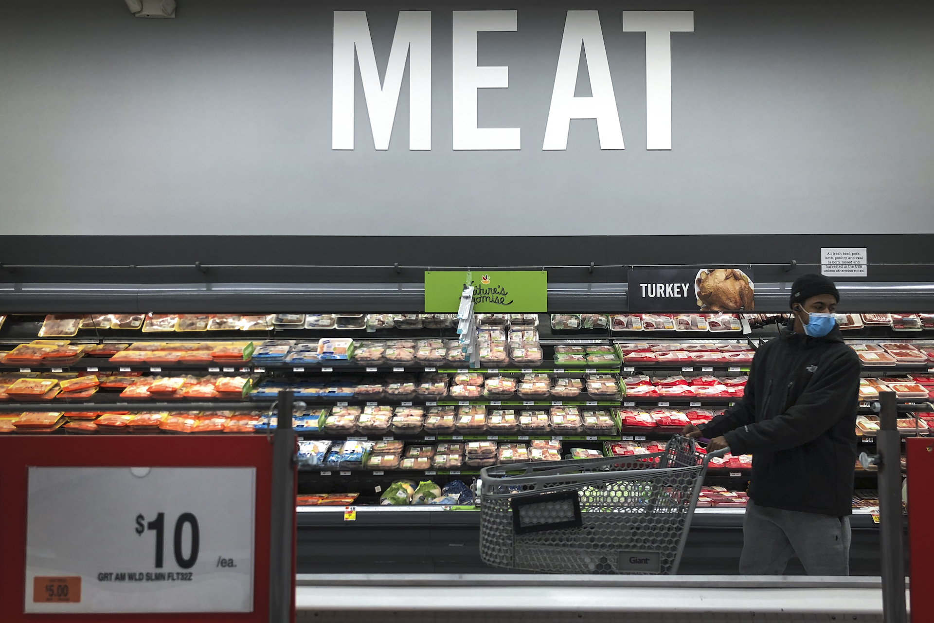 A man pushing a grocery cart stands in front of the meat section of a grocery store.